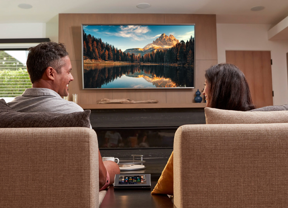 Couple watching a wall-mounted TV with a control tablet for whole home automation in Edgewater