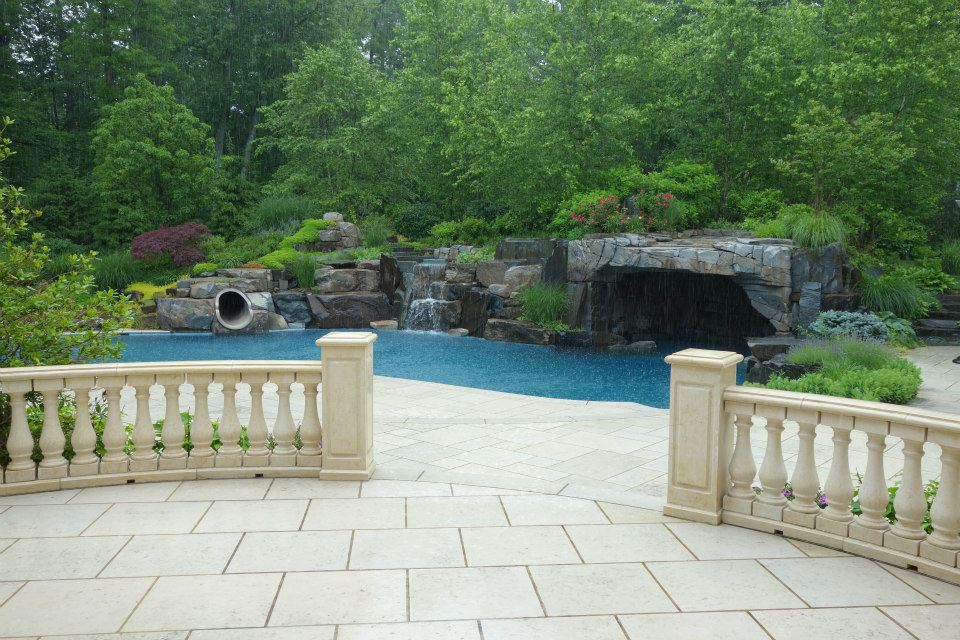 Backyard waterfall pool with a stone patio and outdoor lighting in Saddle River