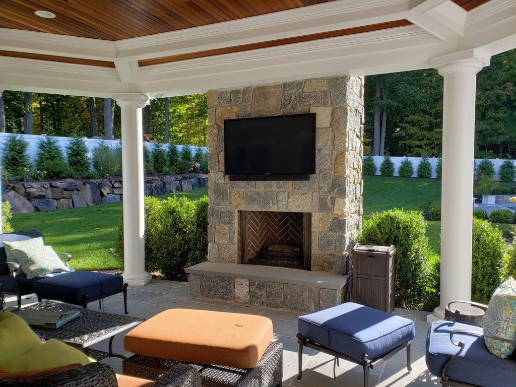 Covered patio with an outdoor TV above a stone fireplace in Greenwich
