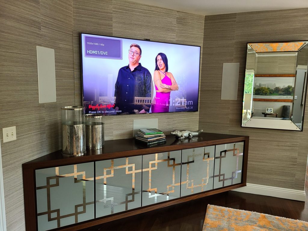 Wall-mounted TV with in-wall speakers above a credenza for a home A/V installation in Franklin Lakes